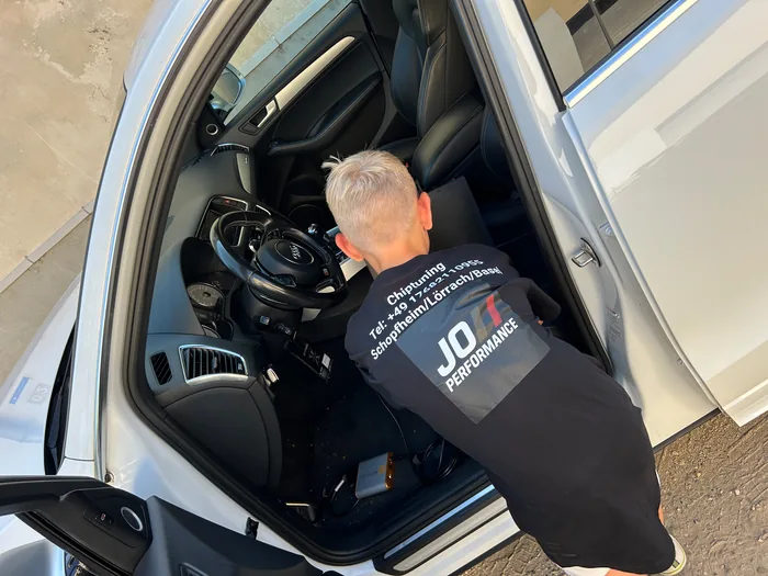 Johann Miller in JO-Performance-Jacke, ins Fahrzeug gebeugt beim Anschließen des Programmiergeräts