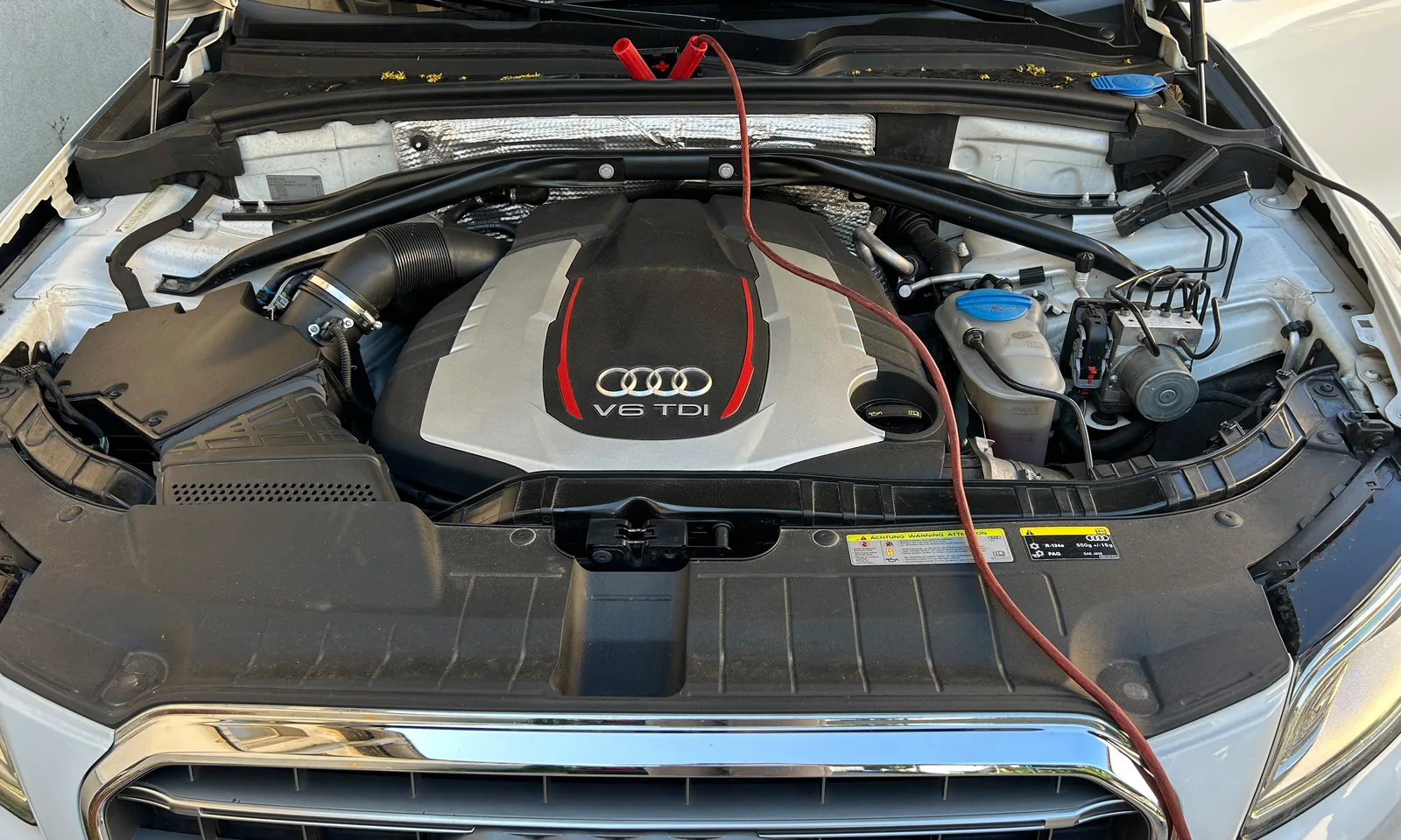 Motorraum eines Audi mit V6-TDI-Abdeckung, angeschlossenem Programmiergerät und Spannungsversorgung