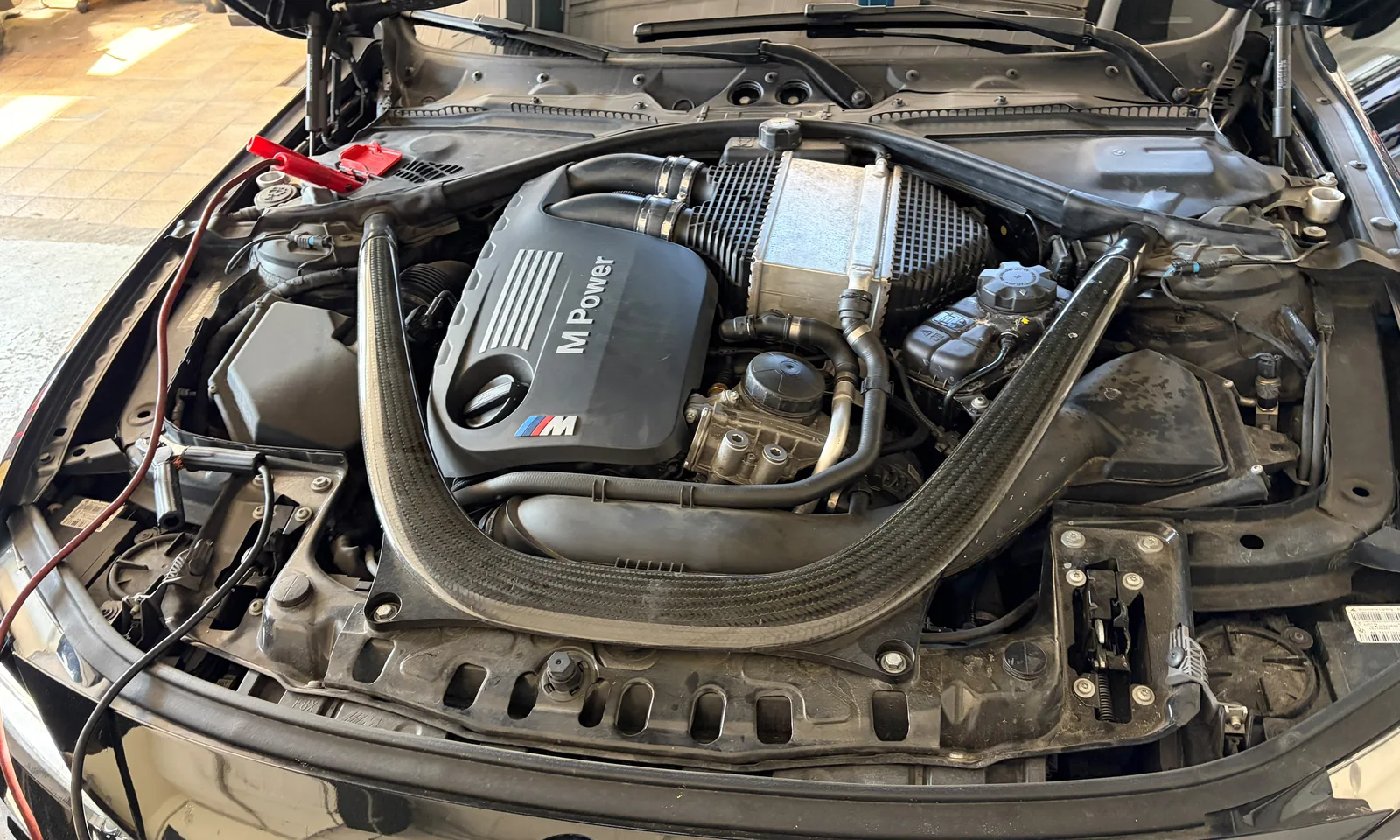 Geöffneter Motorraum eines BMW mit M-Power-Abdeckung und angeschlossenen Messleitungen