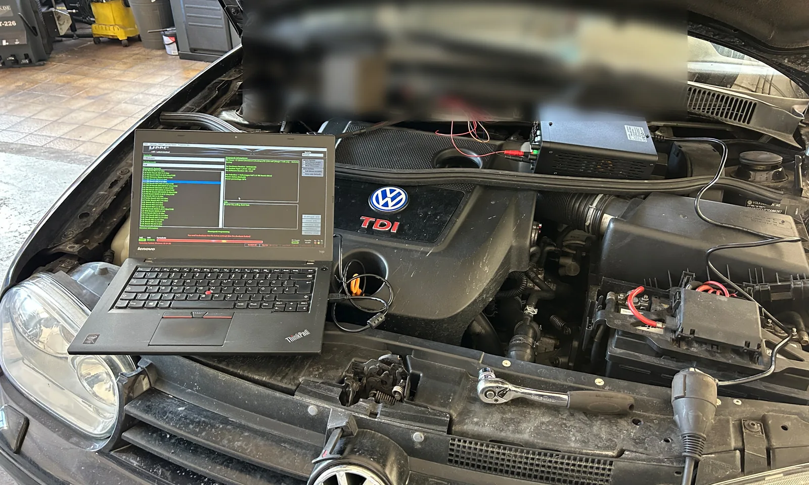 Motorraum eines VW mit TDI-Schriftzug, Laptop auf dem Kühlergrill abgestellt und angeschlossen
