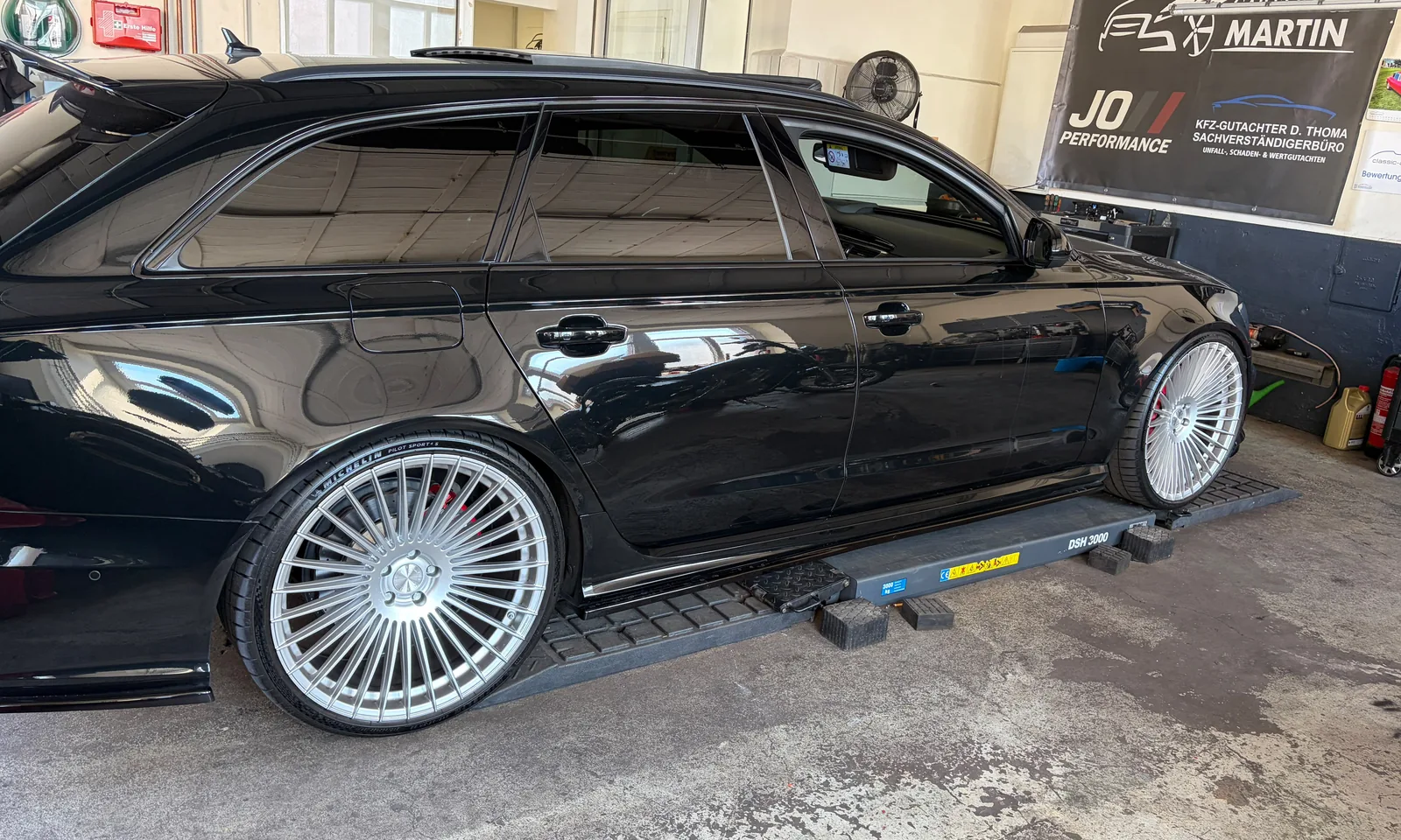 Audi Avant auf Auffahrrampen in der Werkstatt, im Hintergrund die Schilder von JO Performance und der Partnerwerkstatt
